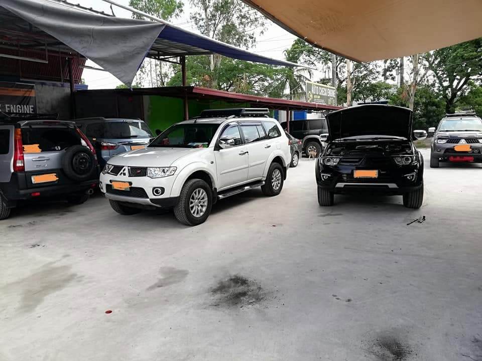 Four SUVs parked under a canopy in the shop yard, one with its bonnet raised
