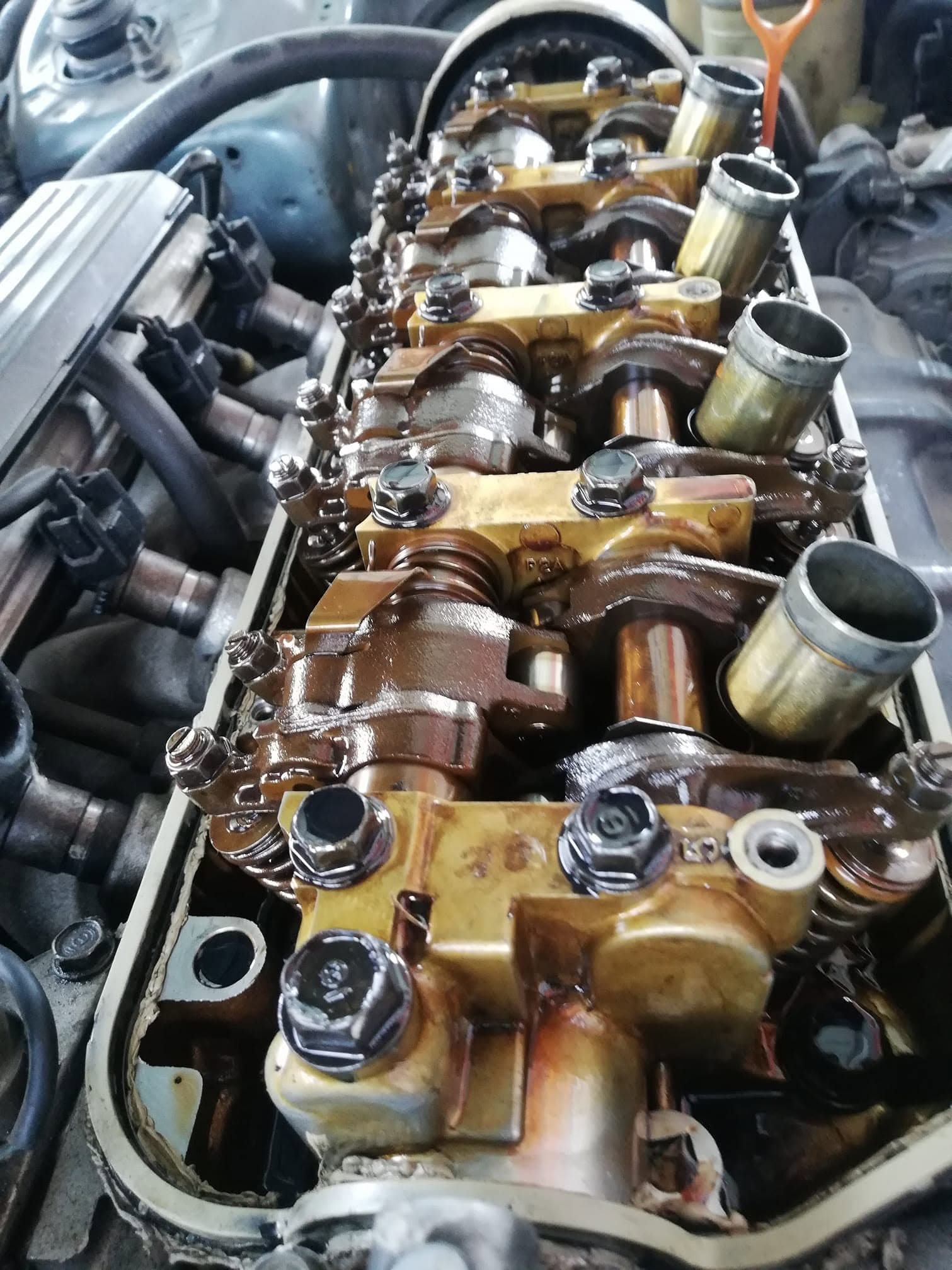 A cylinder head with the valve cover removed, showing rocker shafts and camshaft caps heavily varnished with brown oil deposits