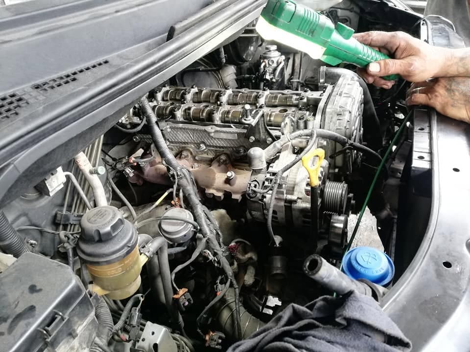 A mechanic pouring oil from a green bottle over the camshafts and rockers of an engine during reassembly