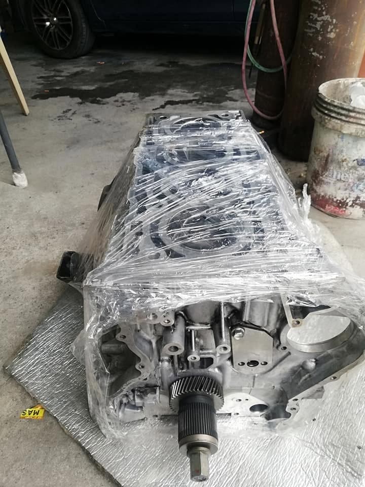A rebuilt engine assembly wrapped in clear plastic film, resting on a mat on the workshop floor