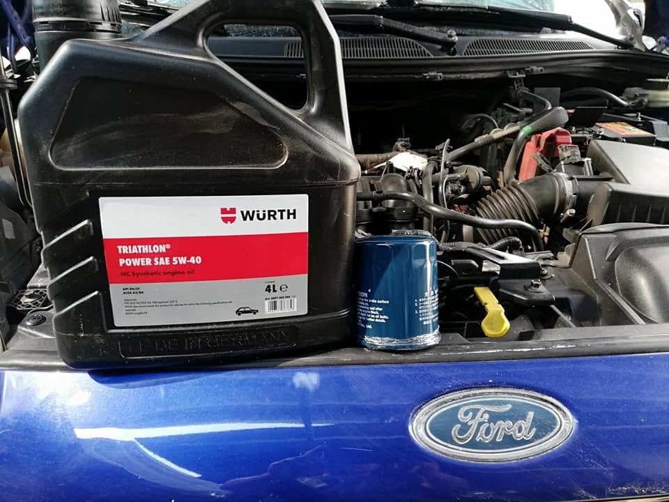 A four litre bottle of Wurth Triathlon Power 5W-40 synthetic oil and a new oil filter resting on the front of a blue Ford