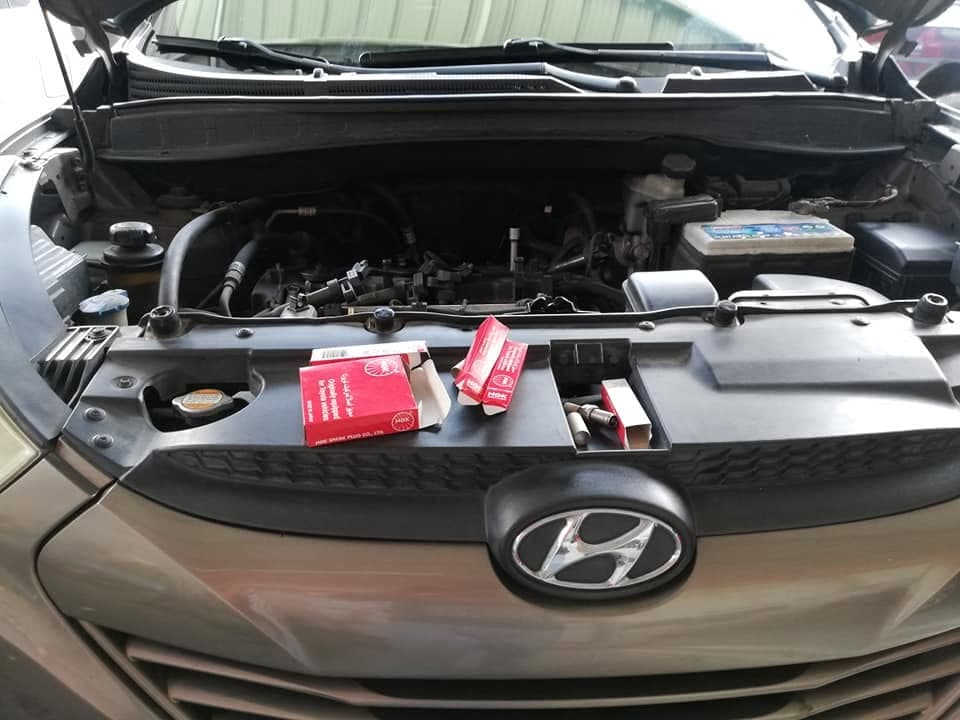 An open Hyundai engine bay with two boxes of NGK spark plugs and loose plugs laid out on the slam panel