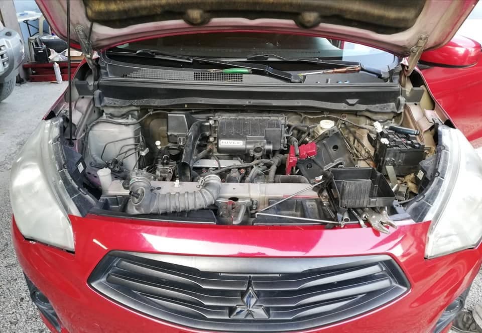 A red Mitsubishi Mirage with its front bumper removed and headlights out, exposing the MIVEC engine and radiator support