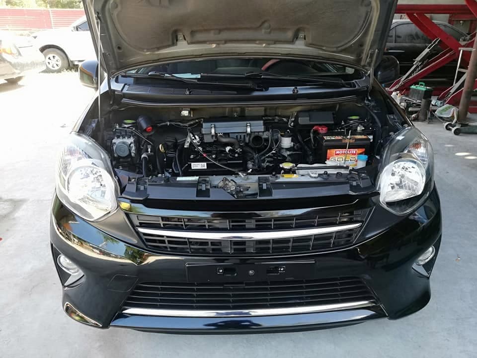 A black Toyota Wigo seen head on with the bonnet up, grille panel removed and the engine bay open