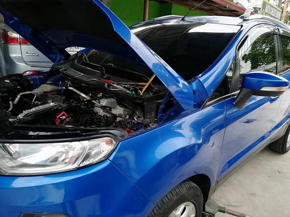 A blue Ford EcoSport parked under cover with its bonnet raised and the engine bay open