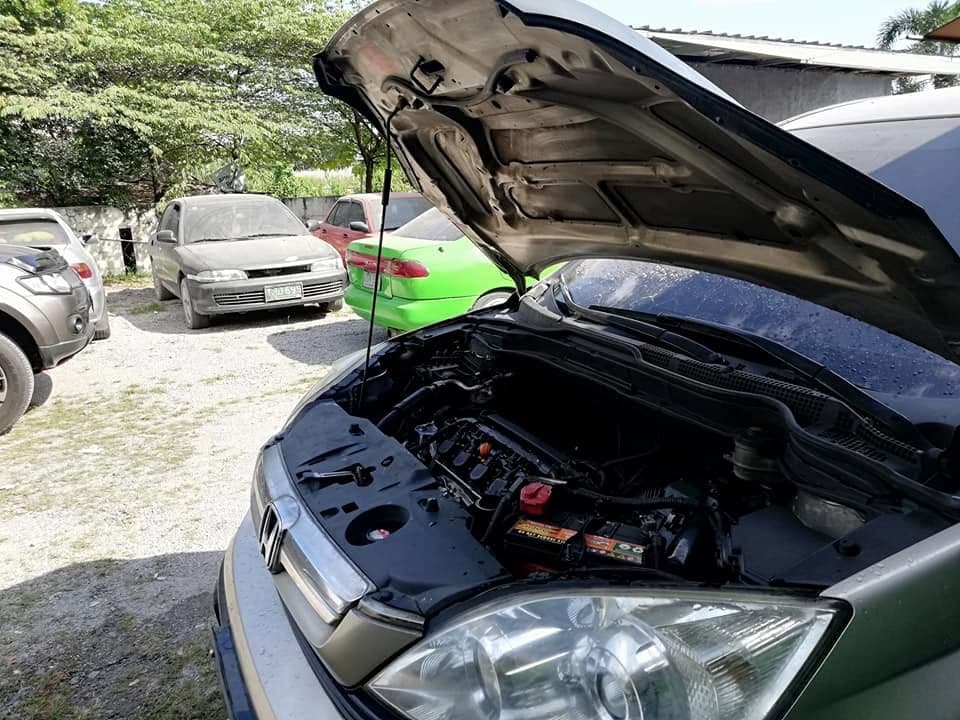 A Honda CR-V with its bonnet propped open in the yard, battery and engine bay visible, other cars parked behind