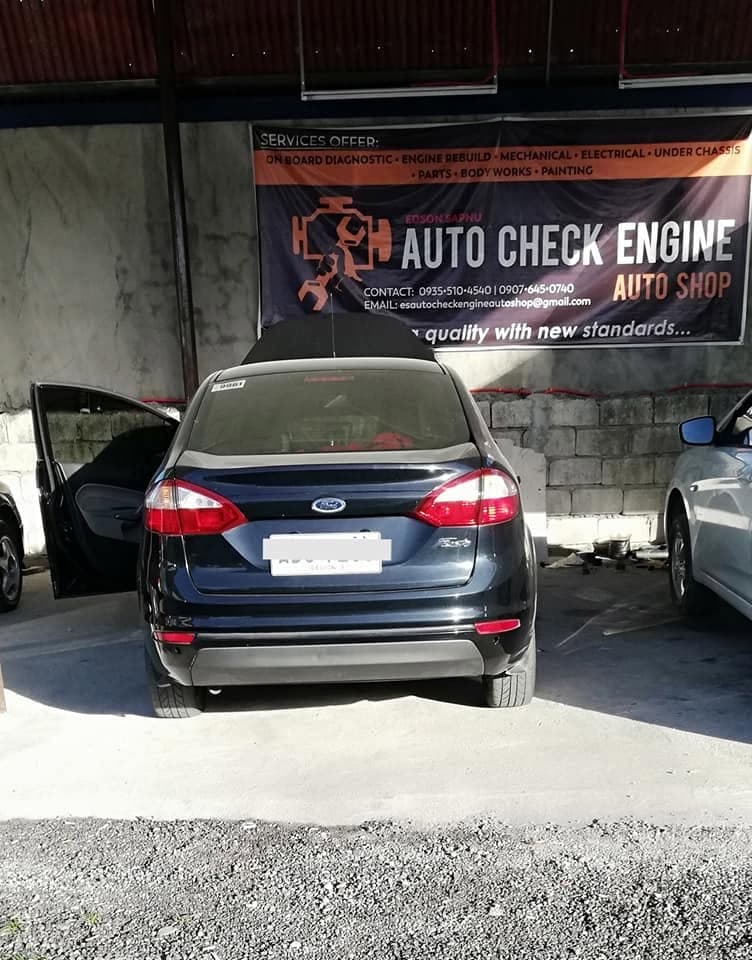 A dark blue Ford Fiesta parked in the bay with a door open, beneath the Auto Check Engine banner listing the shop services